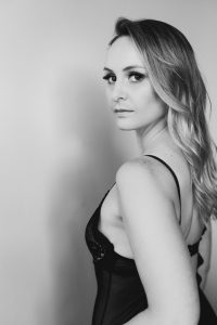 Black and white photo of women in black lingerie looking over her shoulder at the camera.